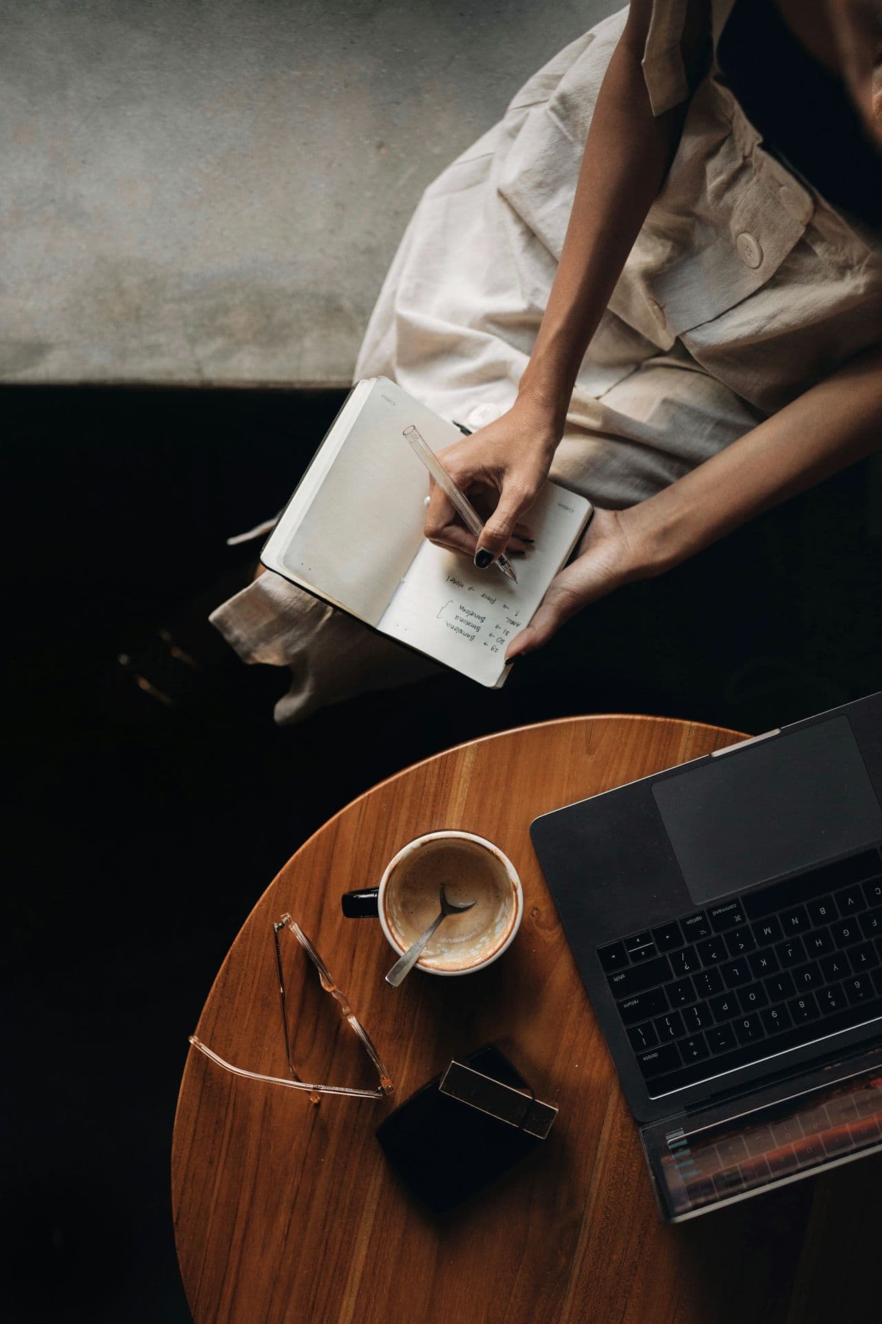 Woman writing in a notebook beside coffee and laptop, symbolizing reflection and planning before an oncology appointment.