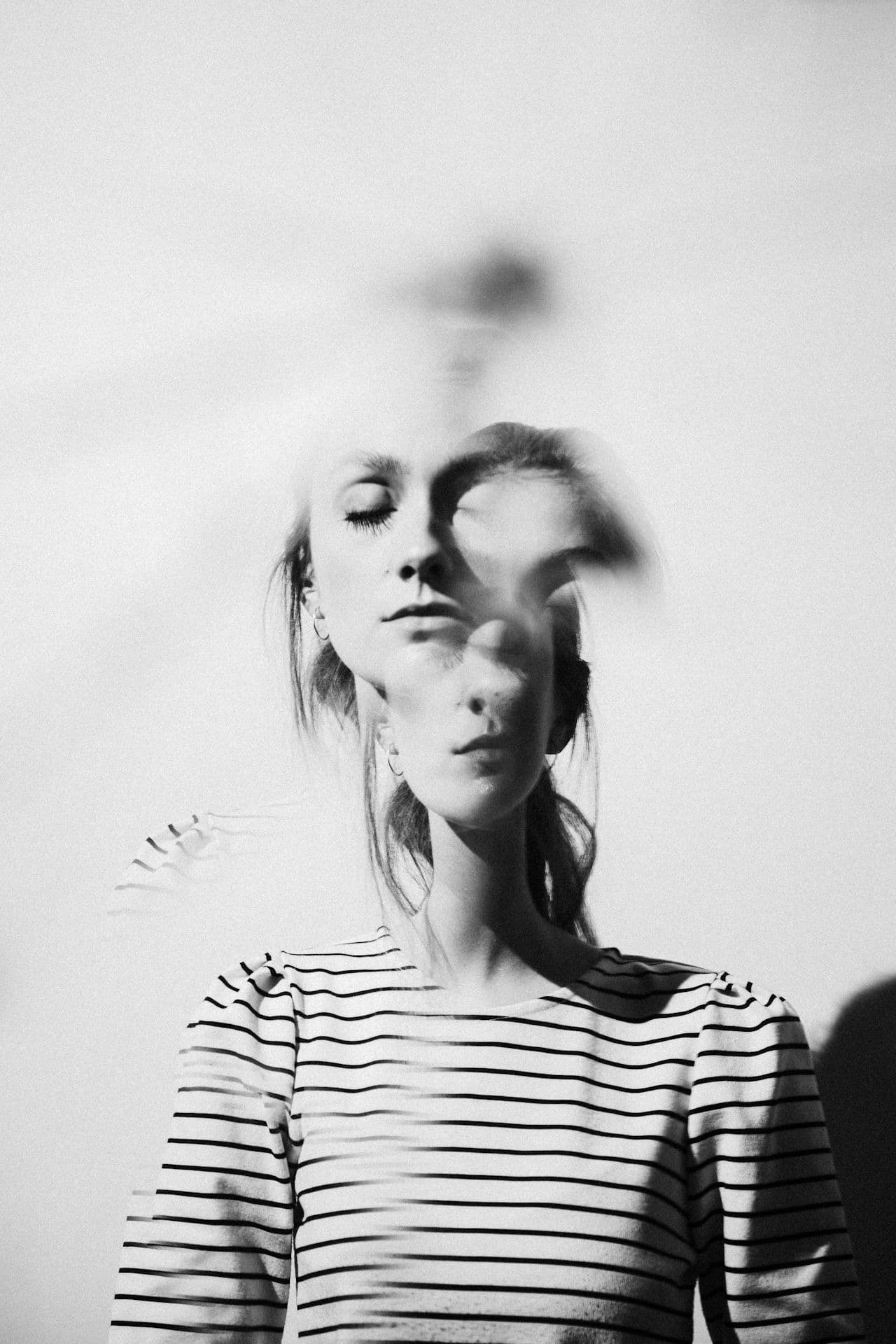 Black-and-white double exposure of a woman with closed eyes, reflecting inner tension and emotion tied to anxiety before cancer scans.
